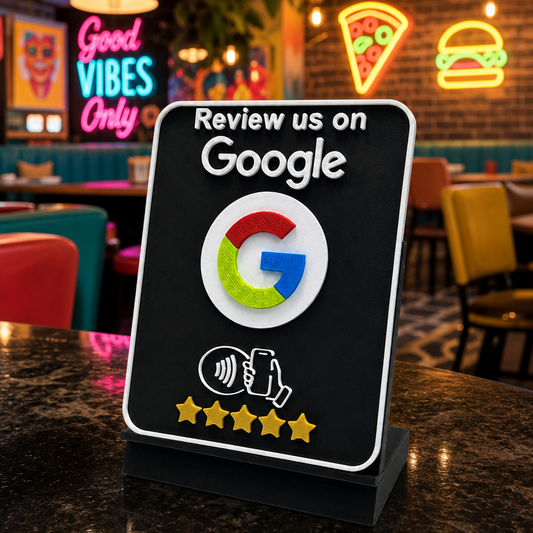 A freestanding black sign on a restaurant counter that reads 'Review us on Google' with the Google logo and a five-star rating graphic, set against a blurred dining environment.